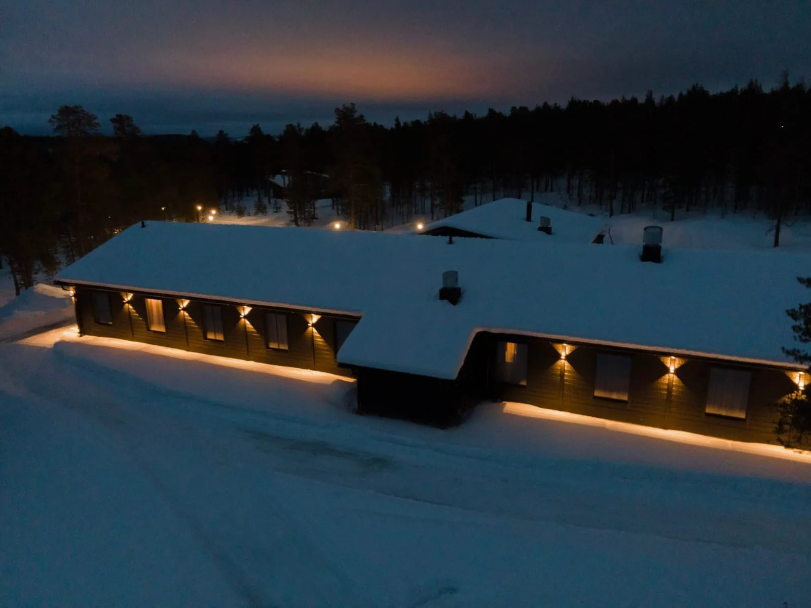 Hotel Kuura photographed above its snow-covered roof at dusk, with forest behind the building.