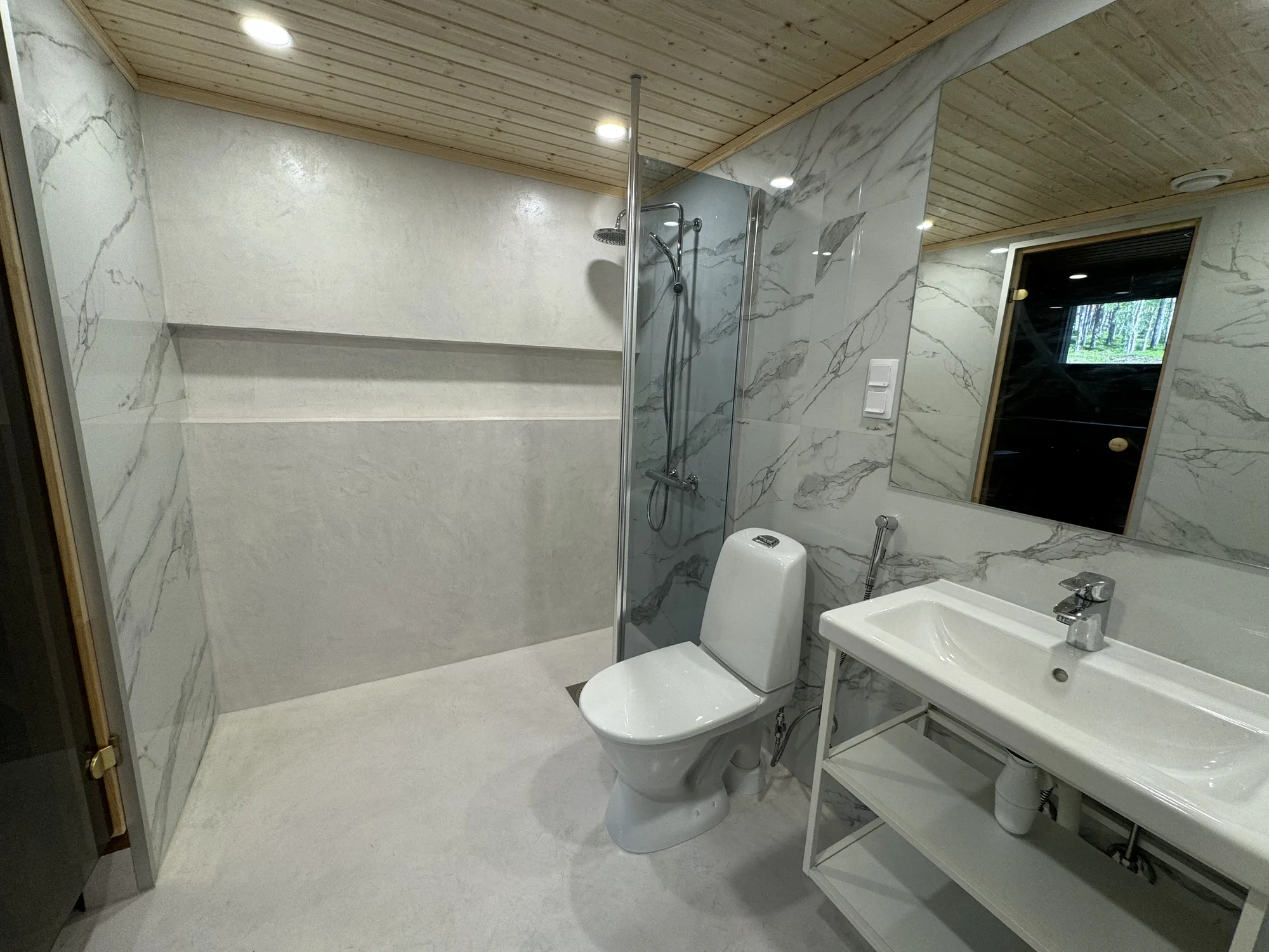 Owl's Nest bathroom: pale stone-patterned walls, an open shower, white basin and a doorway into the timber sauna.