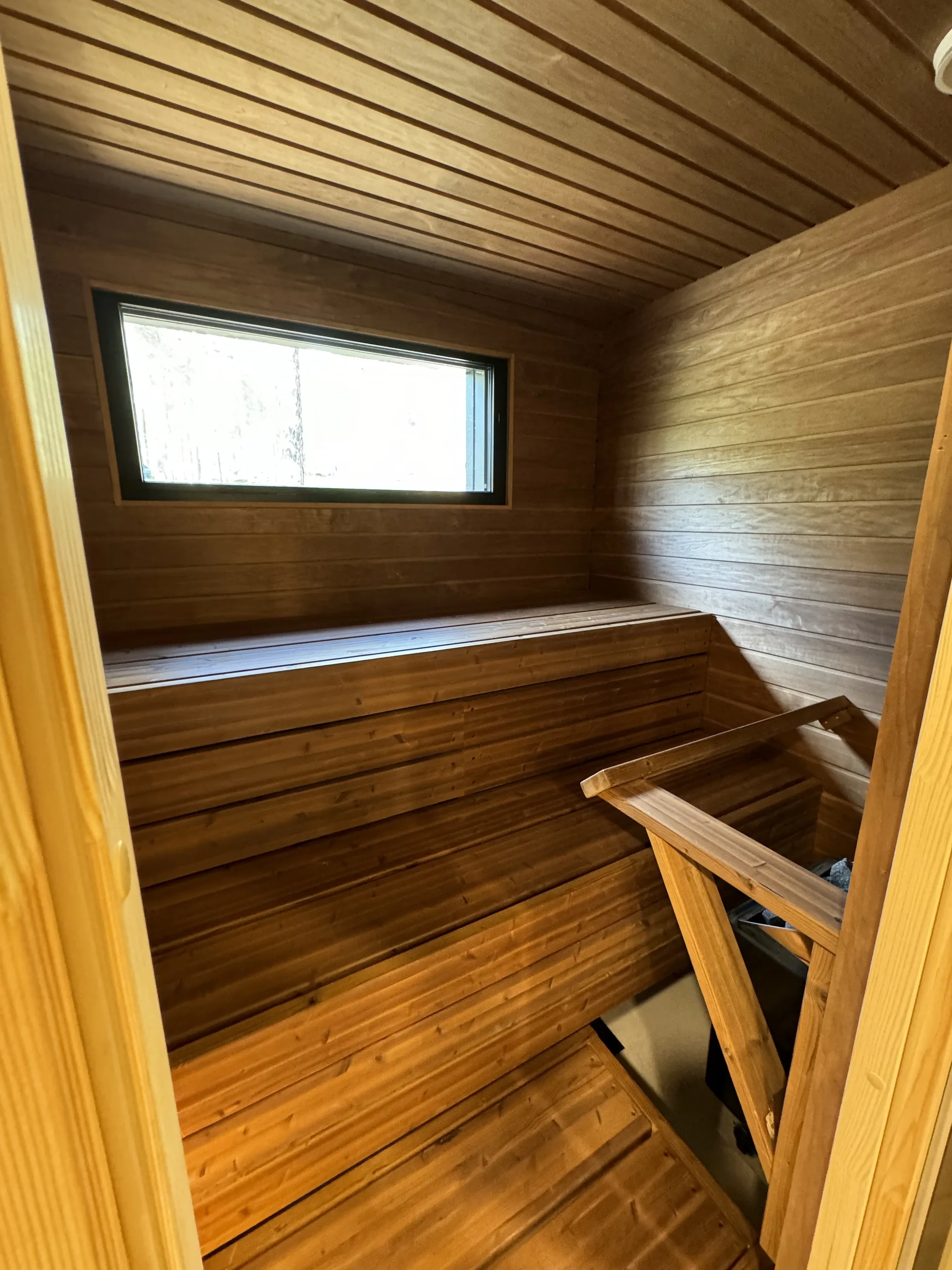 Owl's Nest private sauna: tiered timber benches, timber-panelled walls and a window toward the forest.