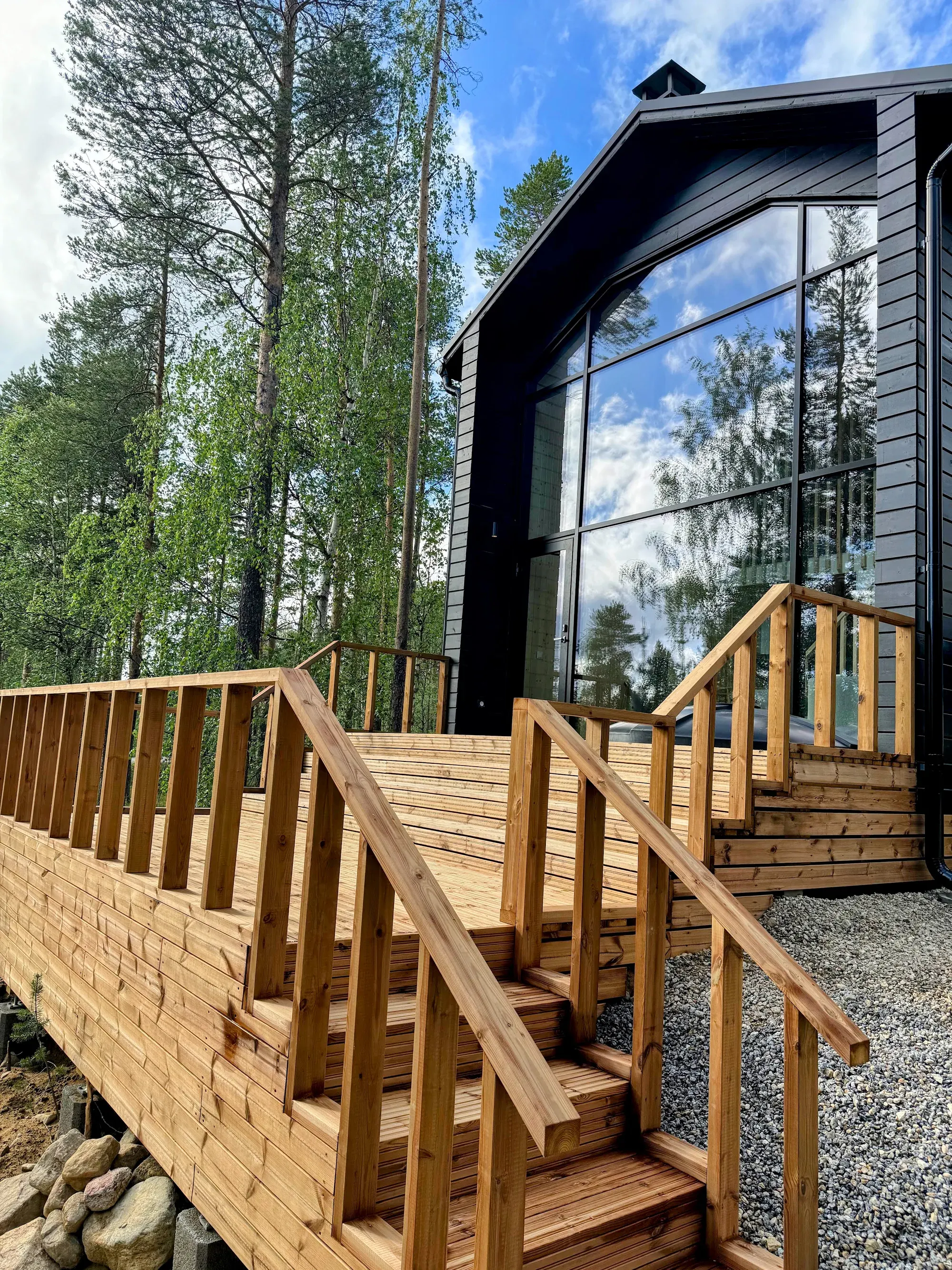Owl's Nest approached by deck stairs, with its black timber gable and tall glass wall among birch and pine trees.