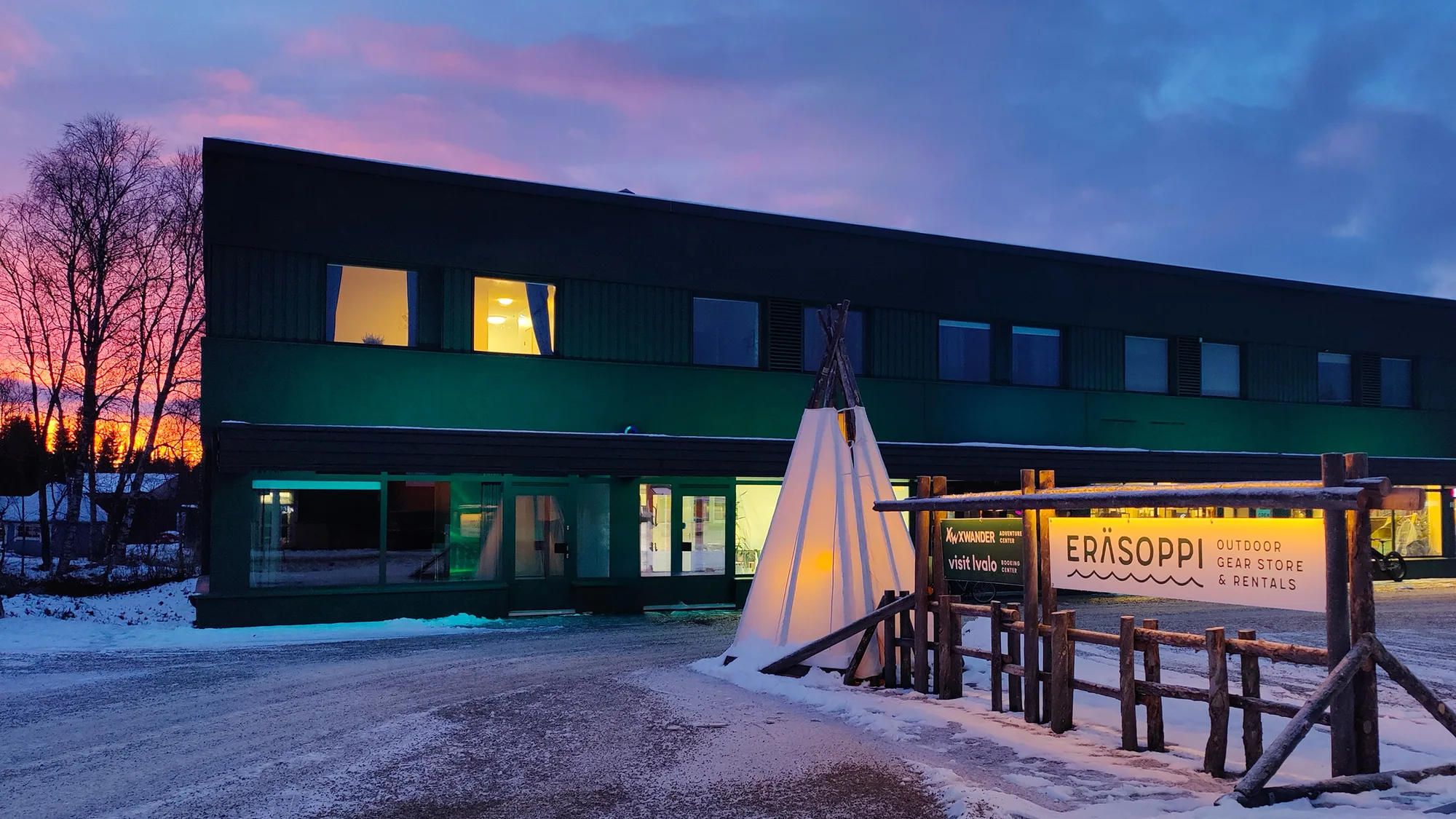 The building at Ivalontie 12 at dusk in snow, with the gear store at street level and apartments above.