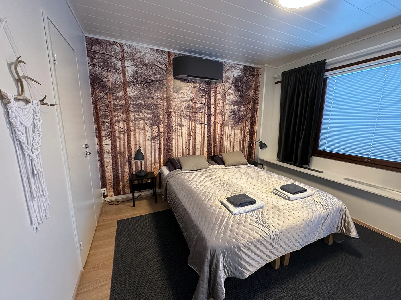 The bed in Pine Studio with a forest painted on the wall behind it.
