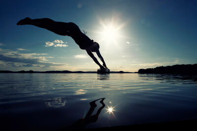 Person diving into Finnish Lapland lake during magical midnight sun